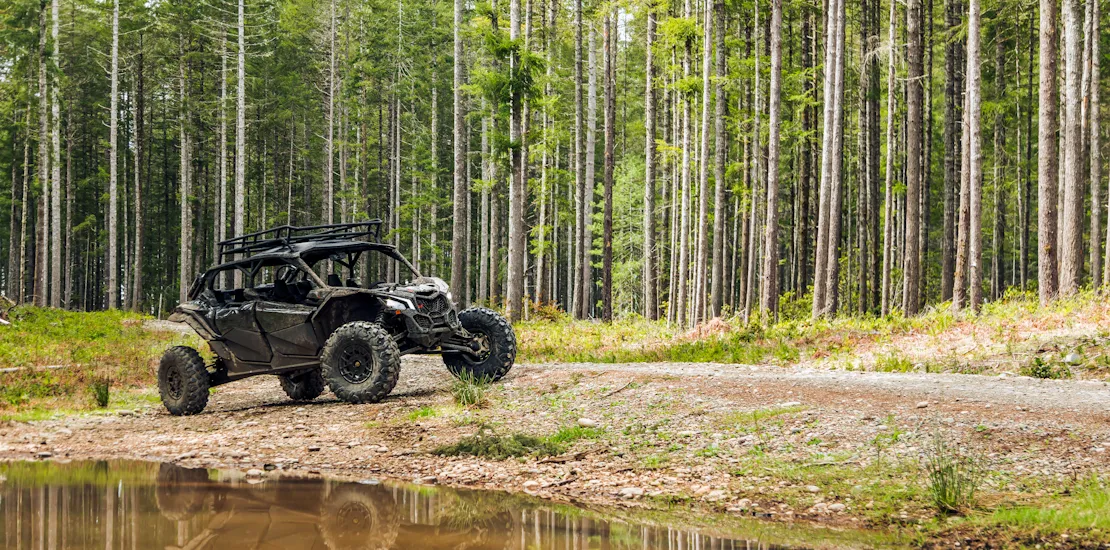 Green ATV going for a dirt road near a lake with a ton of trees behind it